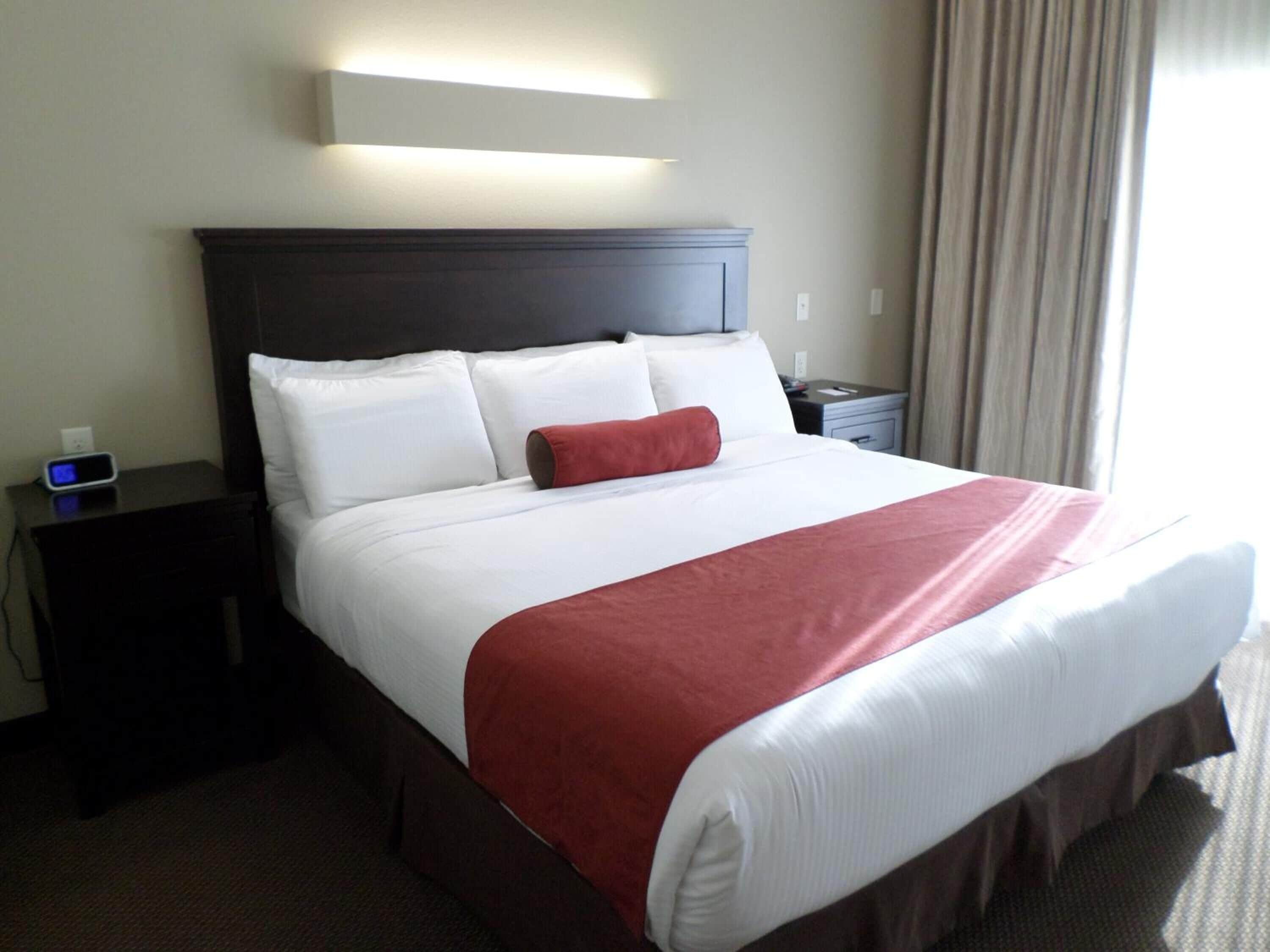 A hotel room with a large bed, a bedside table with a clock, a nightstand, and a wall-mounted light fixture.