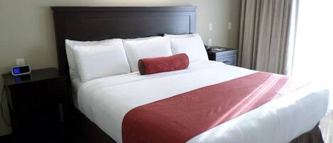 A hotel room with a large bed, a bedside table with a clock, a nightstand, and a wall-mounted light fixture.