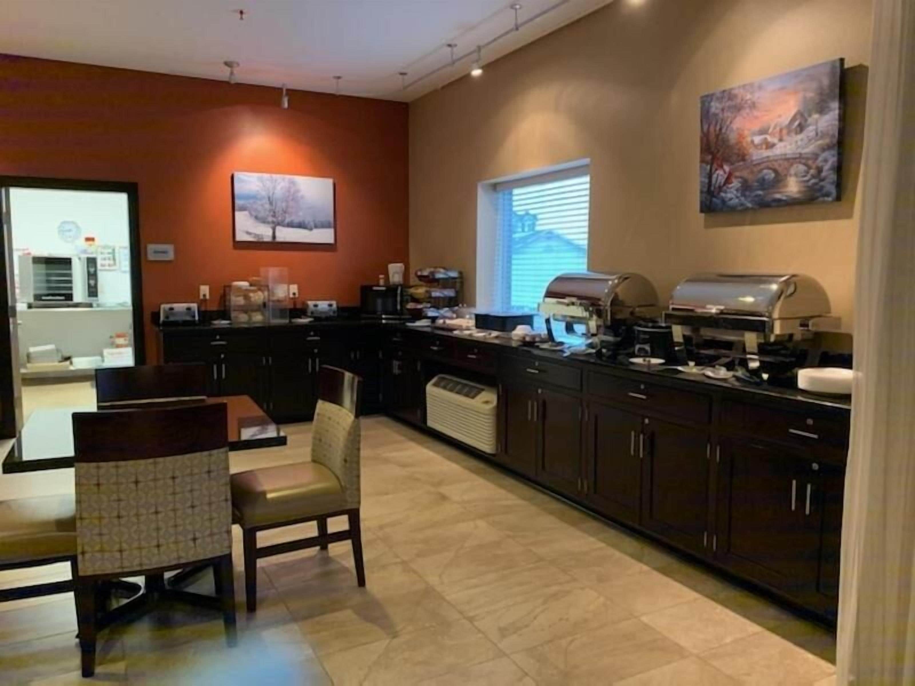 A modern kitchen with dark cabinetry, a central island, and a dining area with a chair.