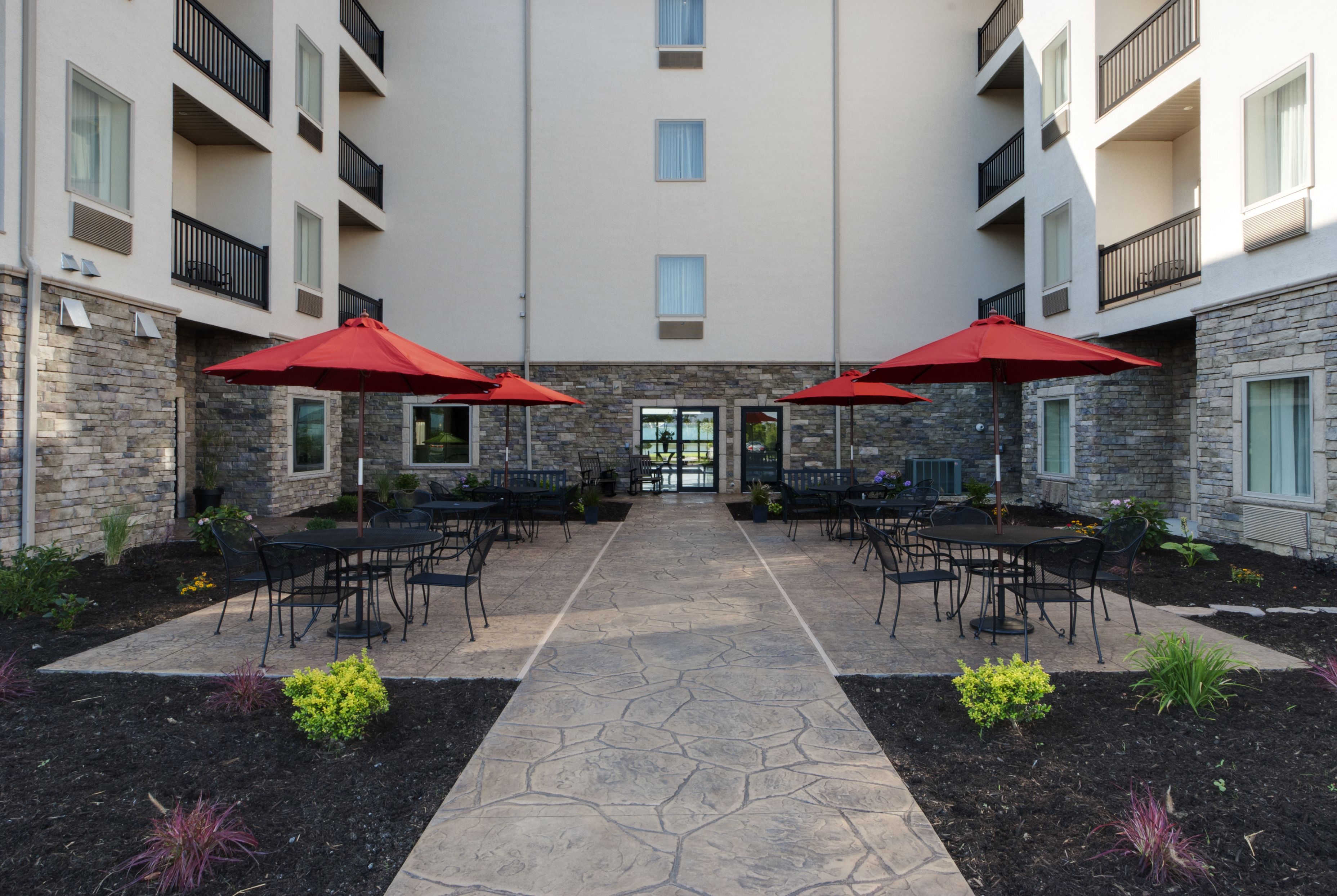 An outdoor patio with stone flooring, black metal chairs, and red umbrellas.