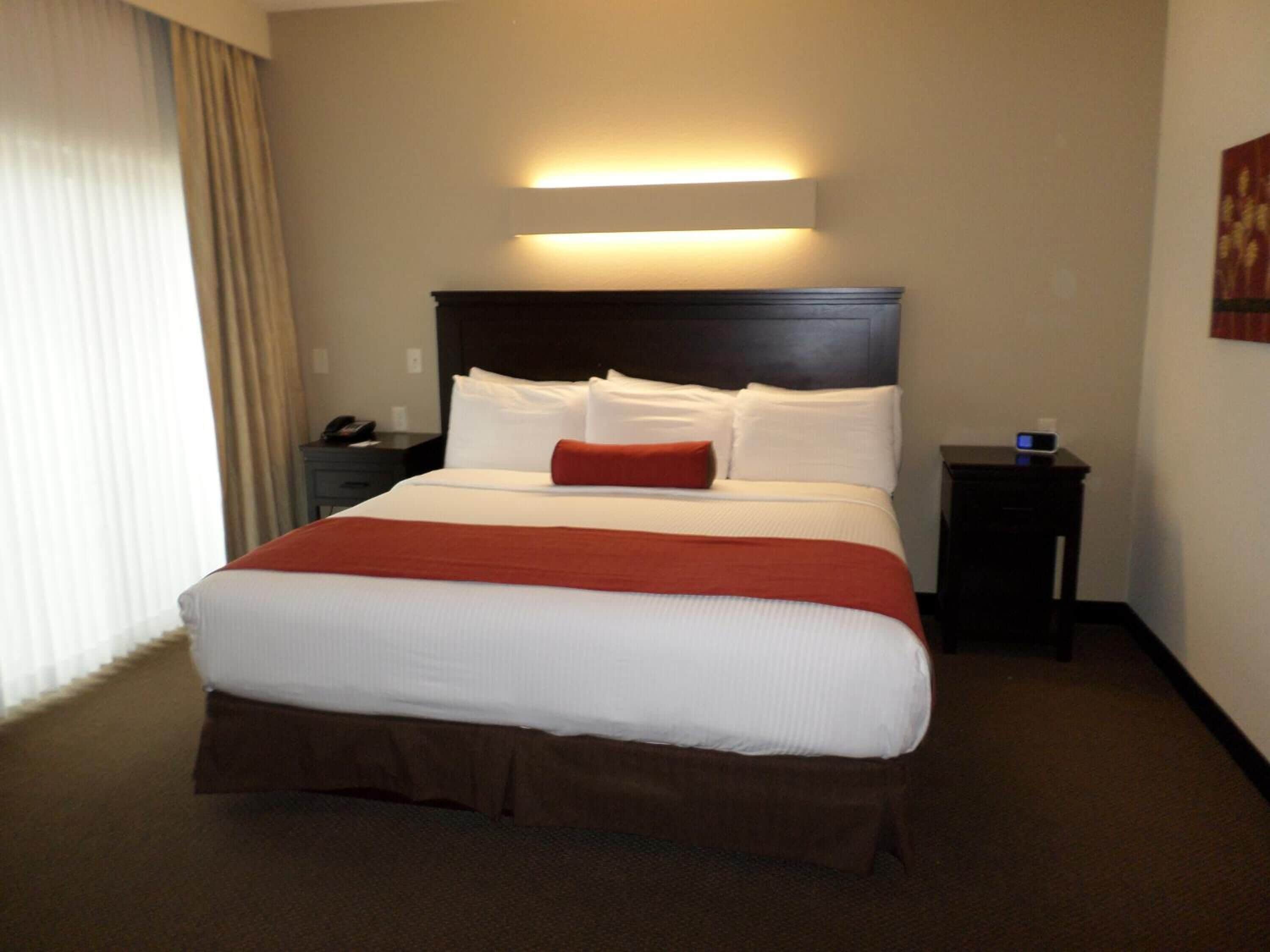 A hotel room with a large bed, a nightstand, a lamp, and a wall-mounted light.