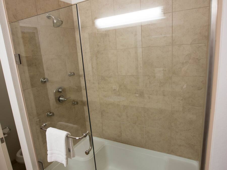 A glass-enclosed walk-in shower with a glass door, a white towel hanging on the door handle, and a light fixture above the shower.