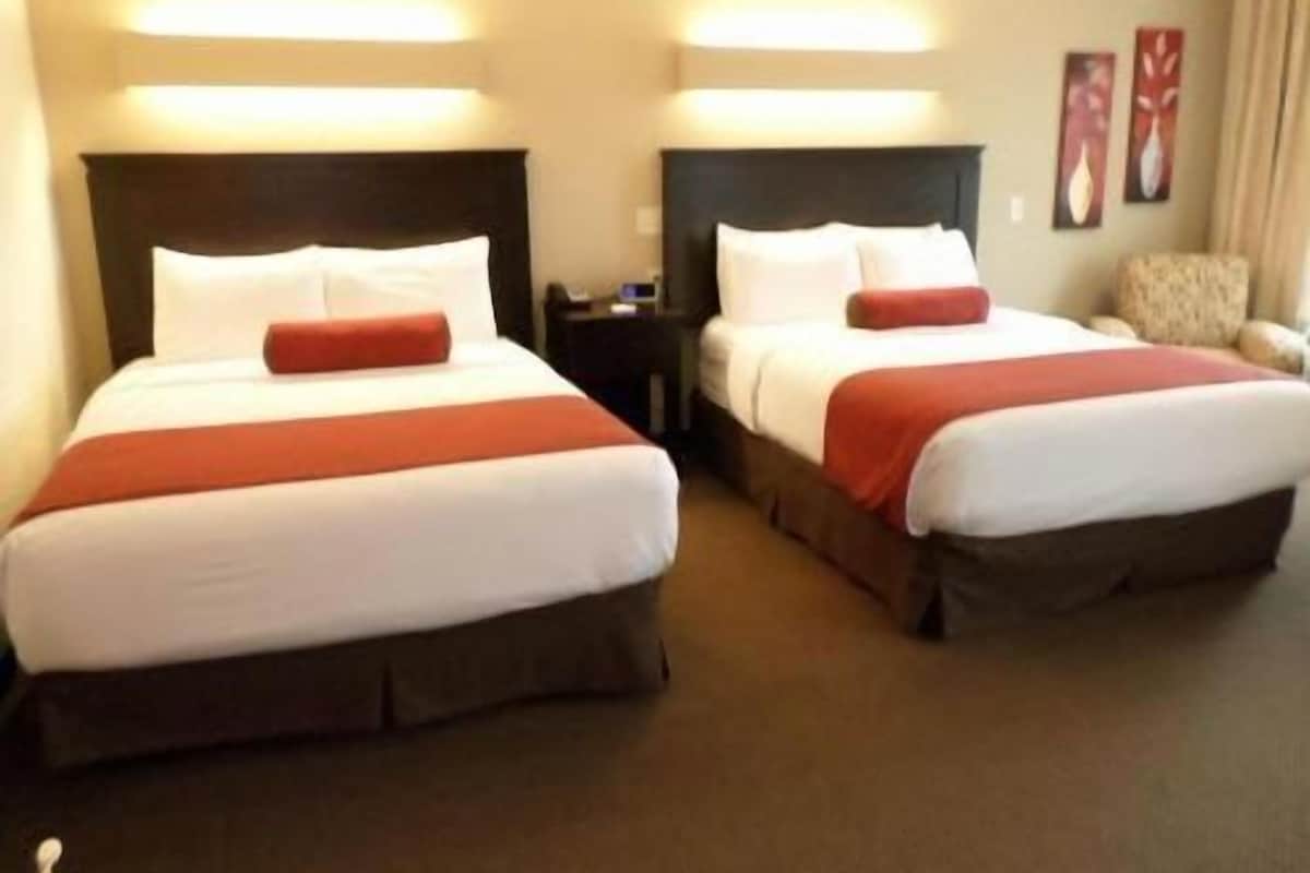 Two twin beds with headboards, a nightstand, and a chair in a hotel room.