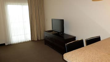 A hotel room with a television on a dresser, a dining table, and two chairs.