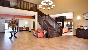 A spacious lobby with a staircase, a chandelier, and a reception desk. - Berlin Grande Hotel (Millersburg)