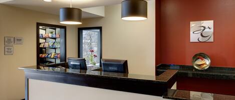 A reception area with a black counter, a glass display case with snacks, a reception desk, and a wall-mounted artwork.