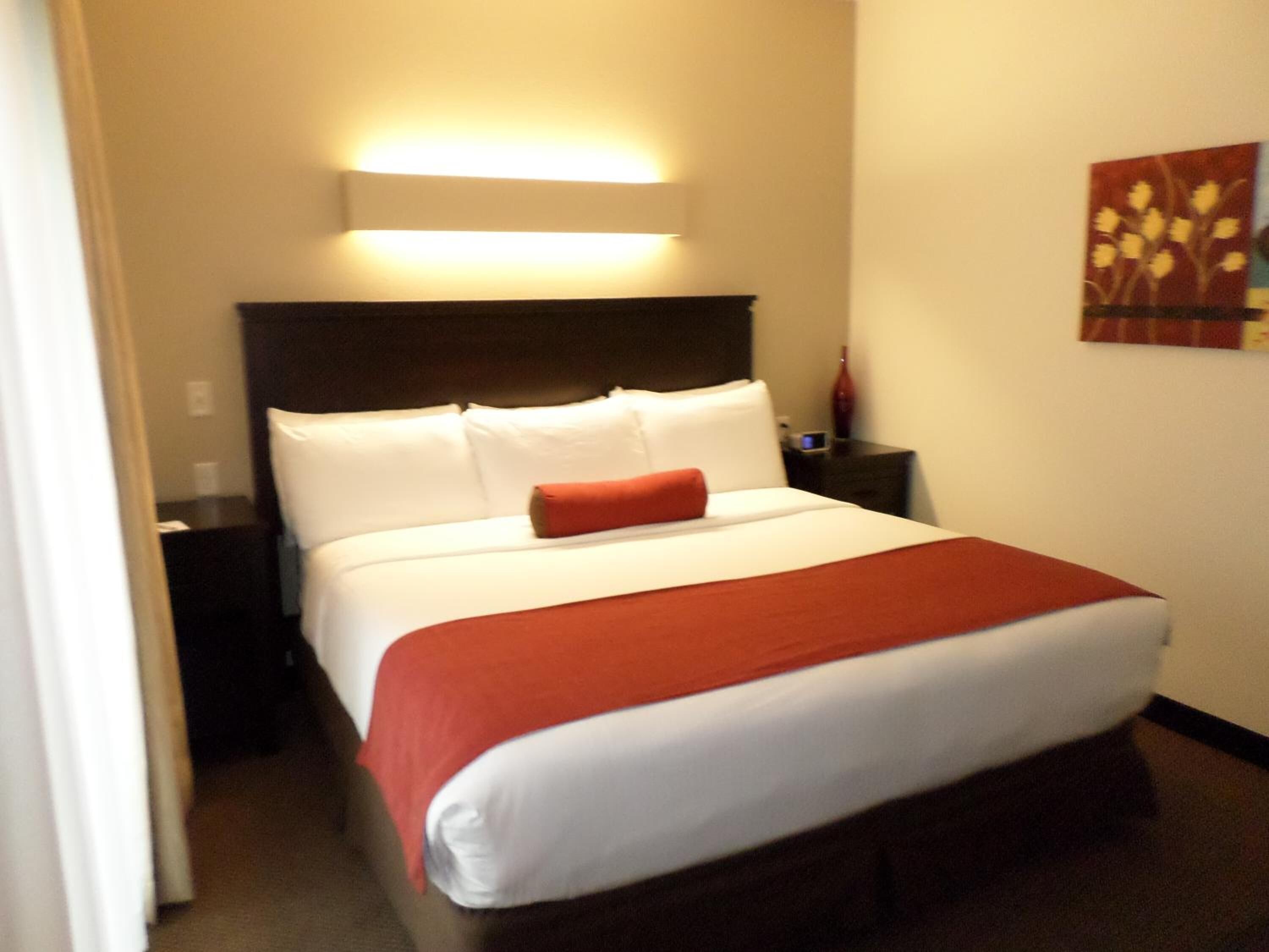 A hotel room with a bed, a nightstand, a lamp, and a wall art piece.