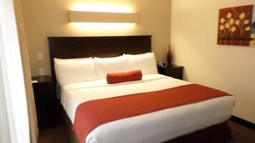 Una habitación de hotel con cama, mesita de noche, lámpara y una obra de arte en la pared.