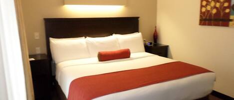 A hotel room with a bed, a nightstand, a lamp, and a wall art piece.
