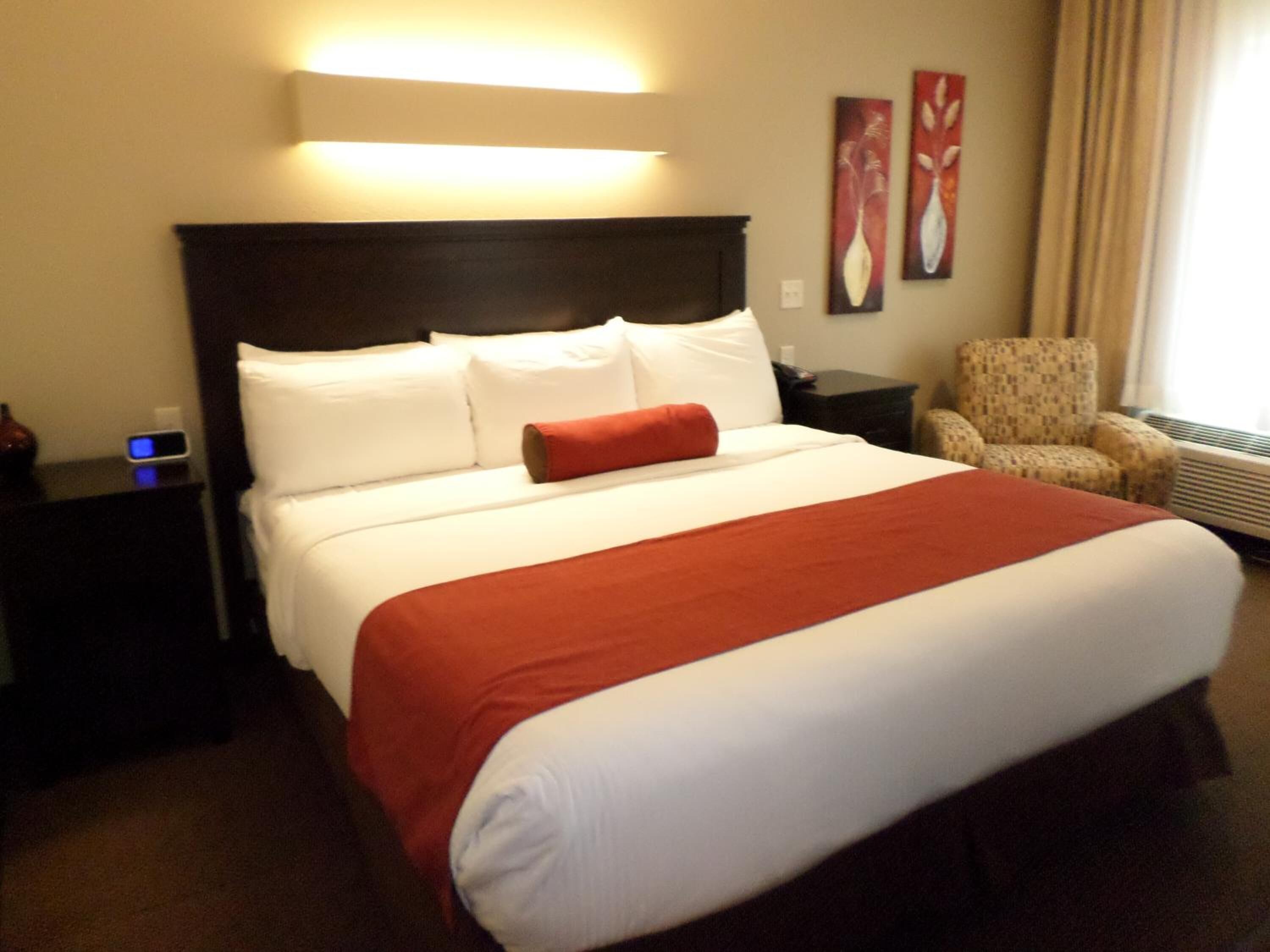 Une chambre d’hôtel avec un grand lit, une table de chevet, une chaise et une lampe fixée au mur.