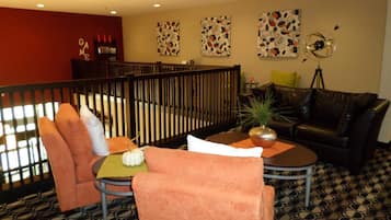 Un rincón lounge acogedor con un sofá de cuero negro, sillas naranjas, una mesita redonda con una planta y una pared decorativa con motivos florales.