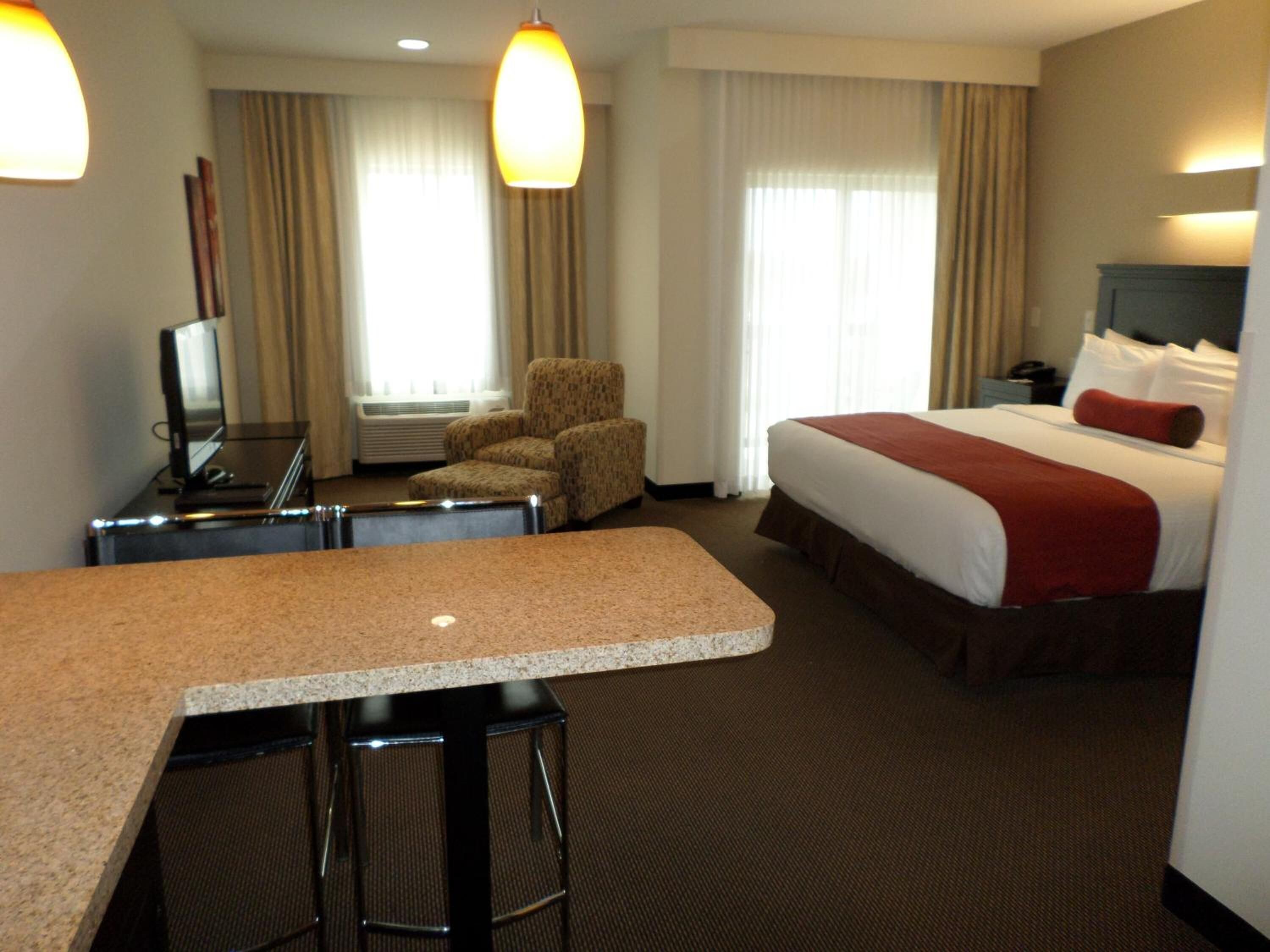 A hotel room with a bed, a desk with two chairs, a television, and a large window with curtains.
