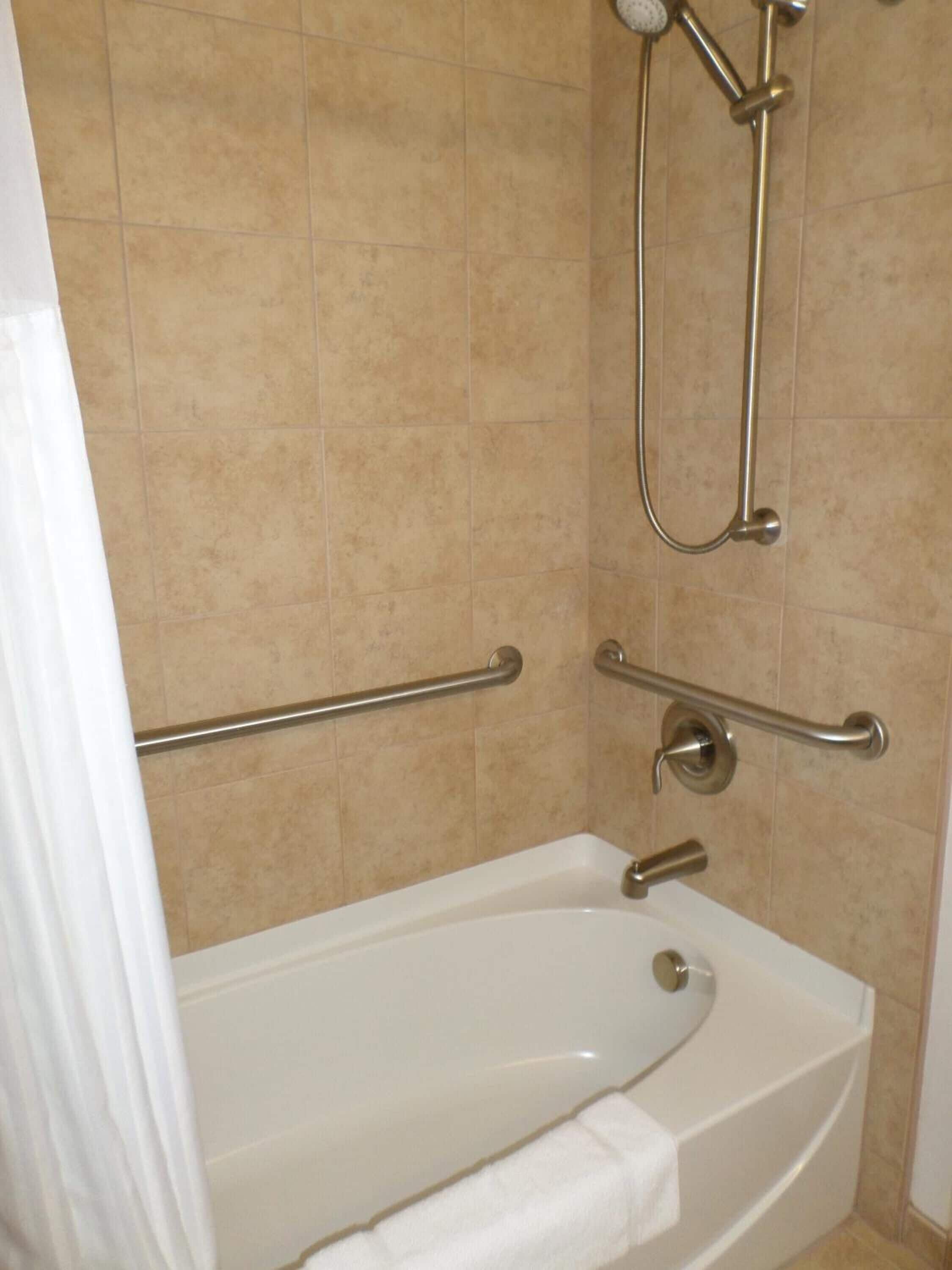 A bathroom with a bathtub, grab bars, and a showerhead.