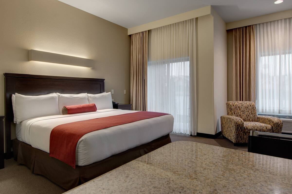Habitación de hotel con una cama grande, una silla, un escritorio y un ventanal con cortinas.