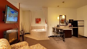 A hotel room with a TV, a sofa, a bathtub, a desk with a chair, and a kitchenette. - Berlin Grande Hotel (Millersburg)