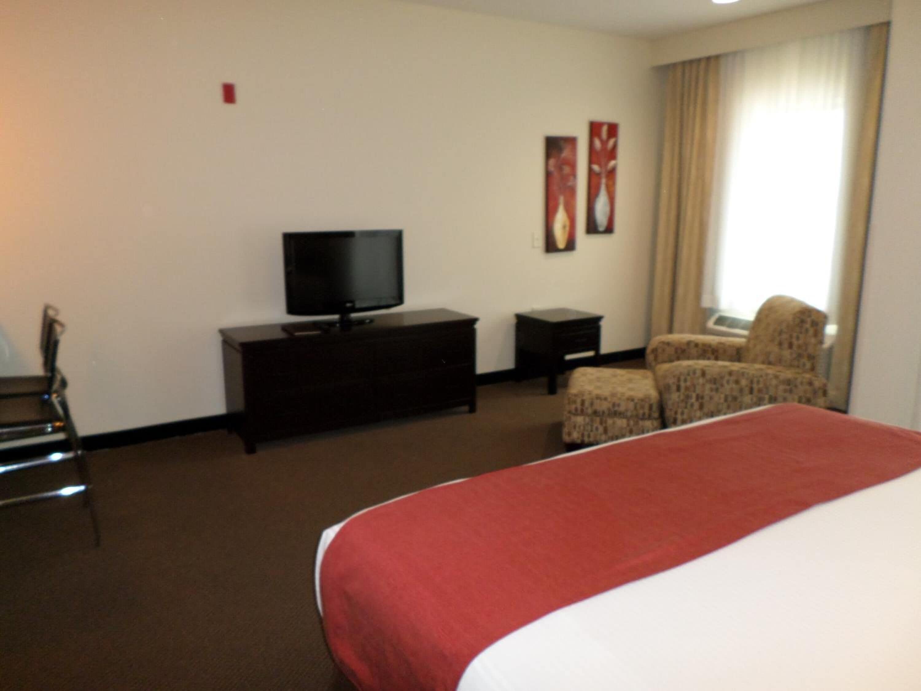 A hotel room with a bed, a television on a dresser, a chair, and a window with curtains.