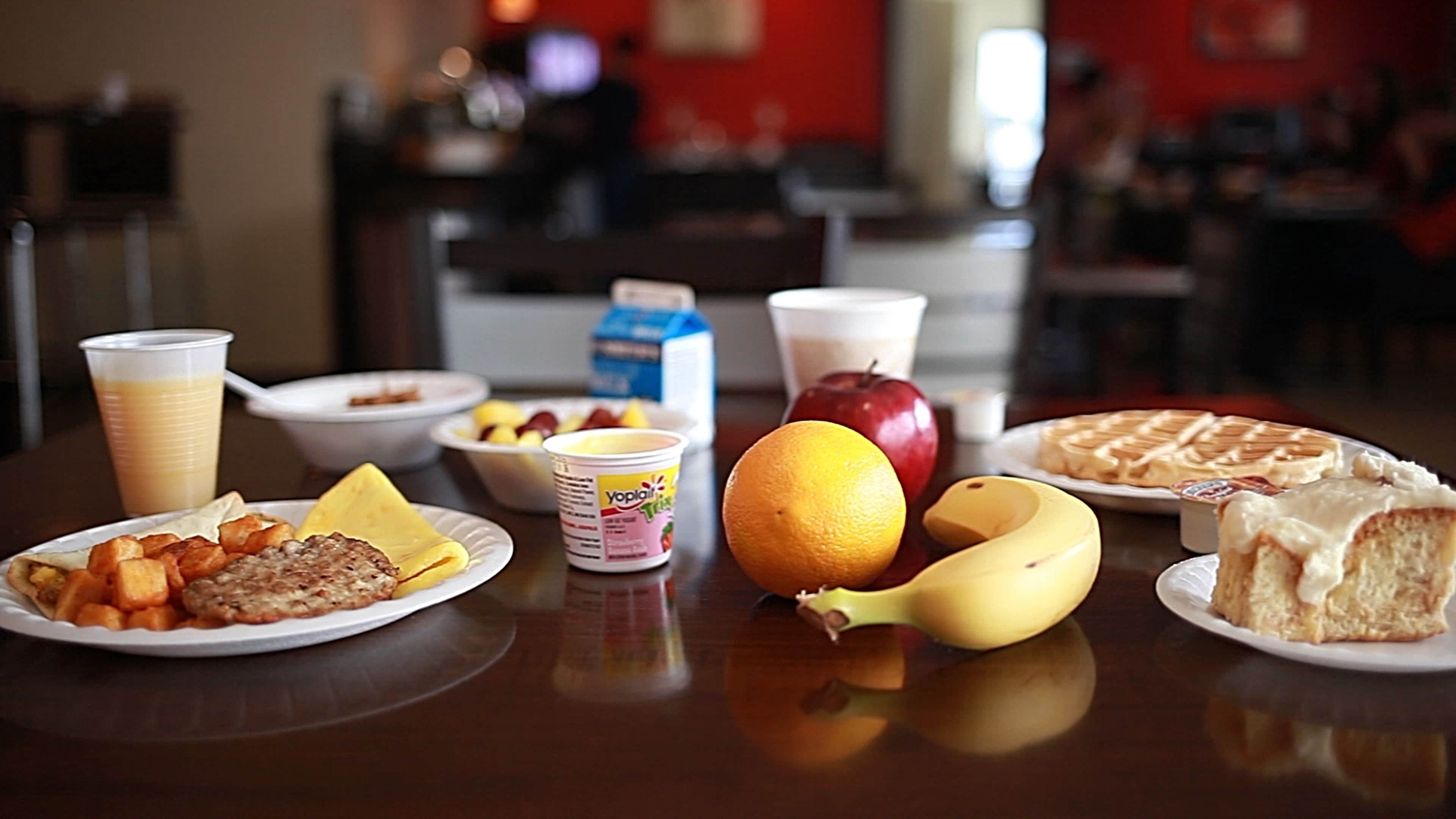 Une table de petit-déjeuner avec divers aliments, notamment des crêpes, des œufs, des toasts et des fruits comme des pommes et des bananes.