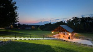 A rustic pavilion with picnic tables and string lights, surrounded by a well-maintained lawn and a stone pathway. - Berlin Grande Hotel (Millersburg)