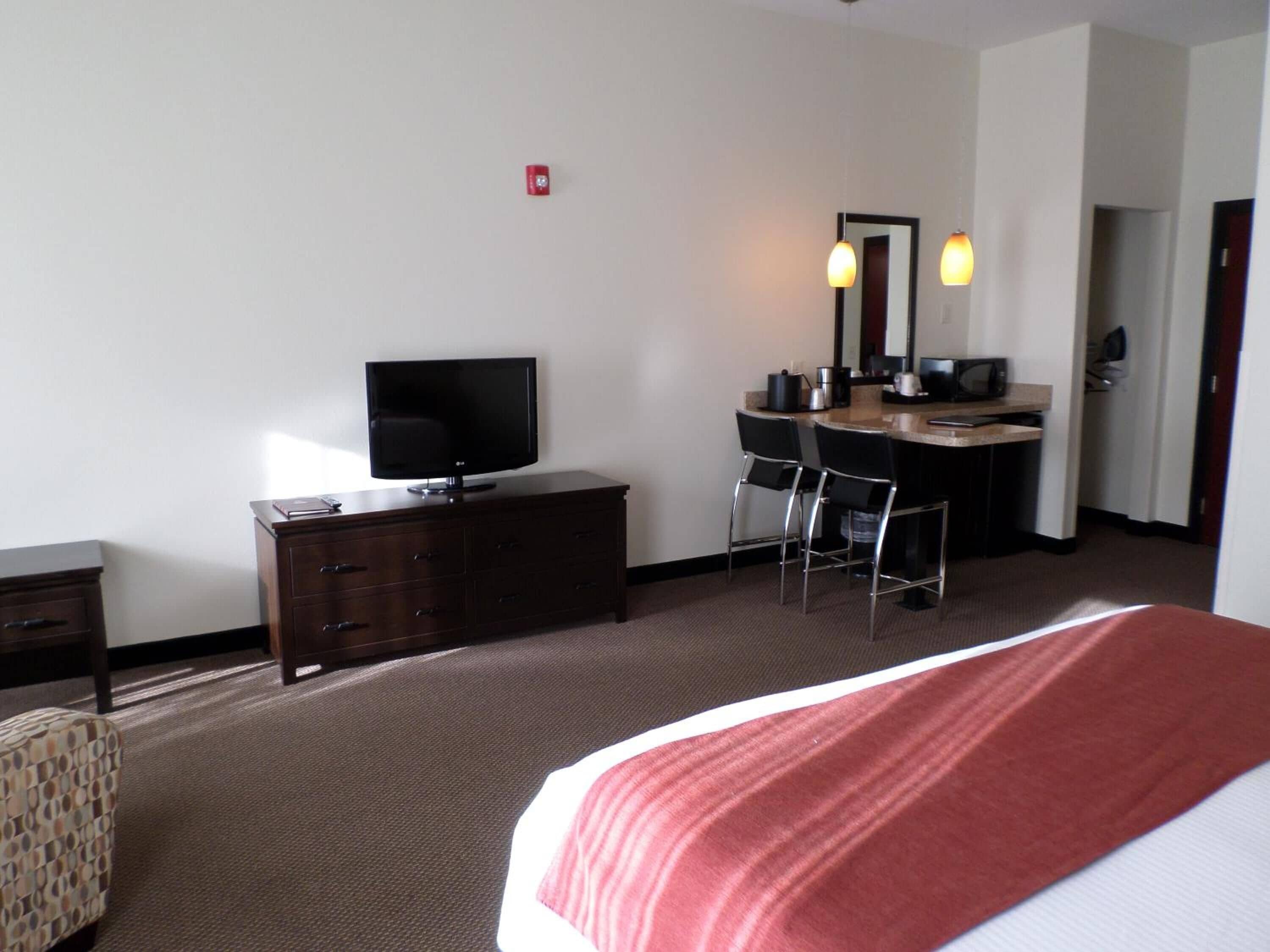 A hotel room with a bed, a TV on a dresser, a desk with a chair, and a microwave.