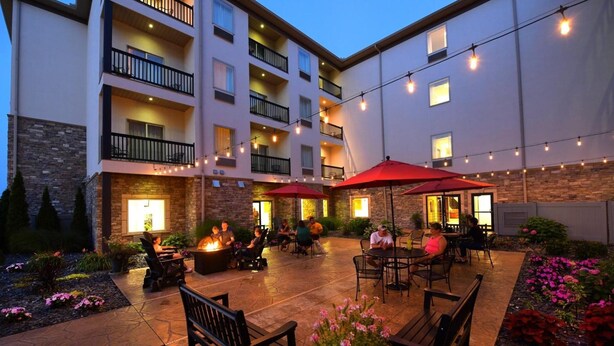 An outdoor patio area with seating and a fire pit, surrounded by a building with multiple balconies and string lights. - Berlin Grande Hotel (Millersburg)