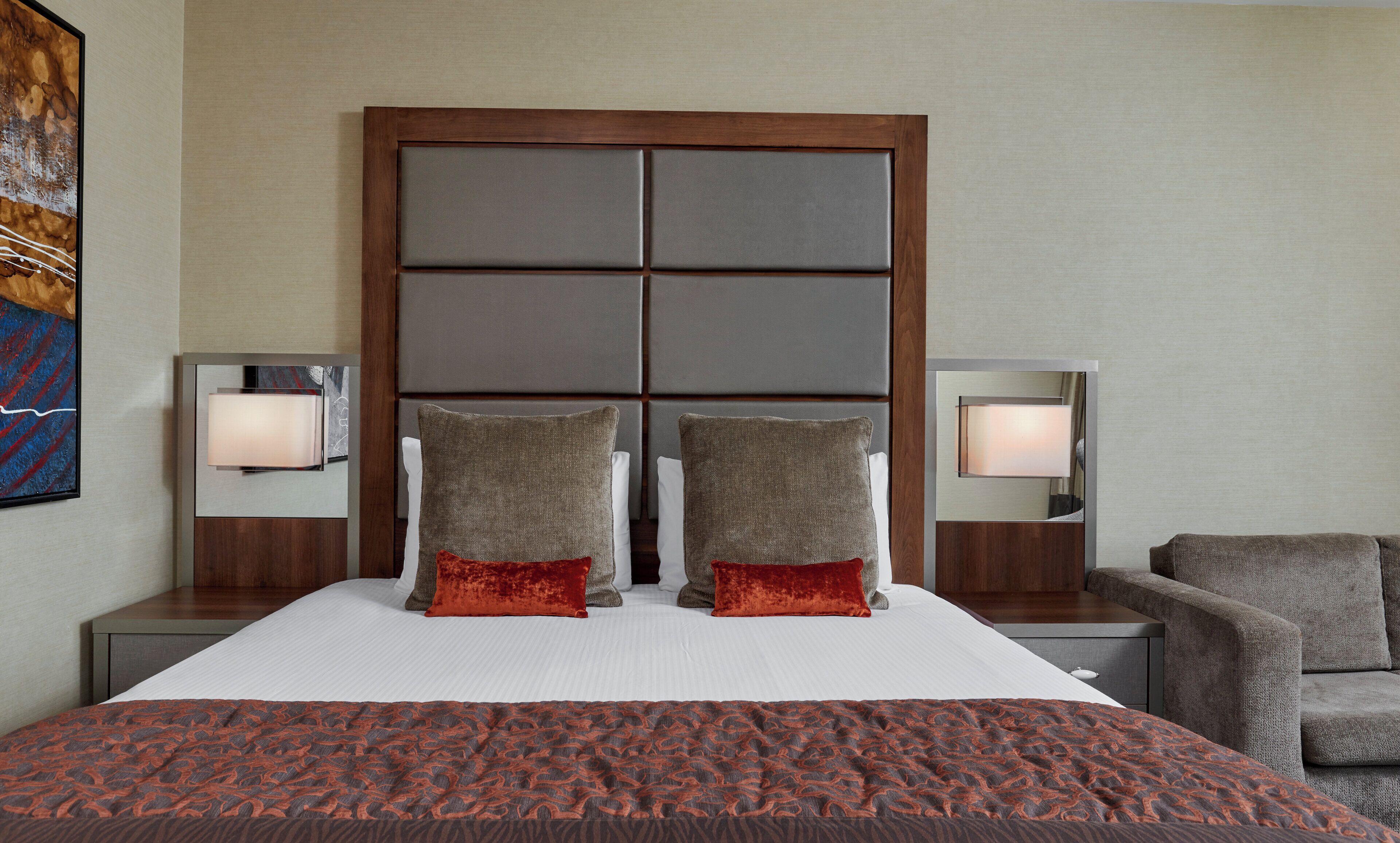 A hotel room with a large bed, two nightstands, a chair, and a painting on the wall.