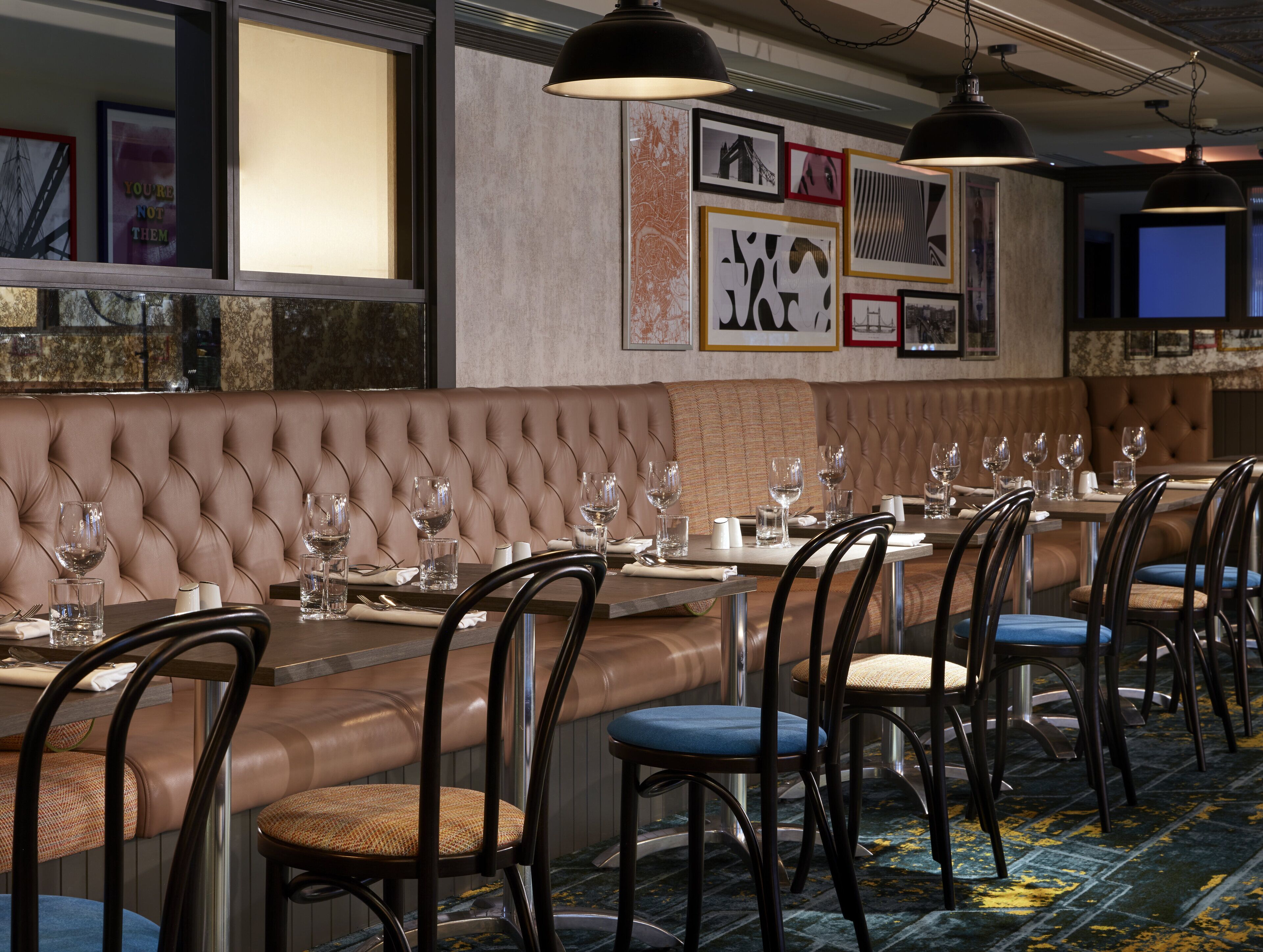 A restaurant with a long, cushioned bench seating area, tables with chairs, and framed artwork on the walls.