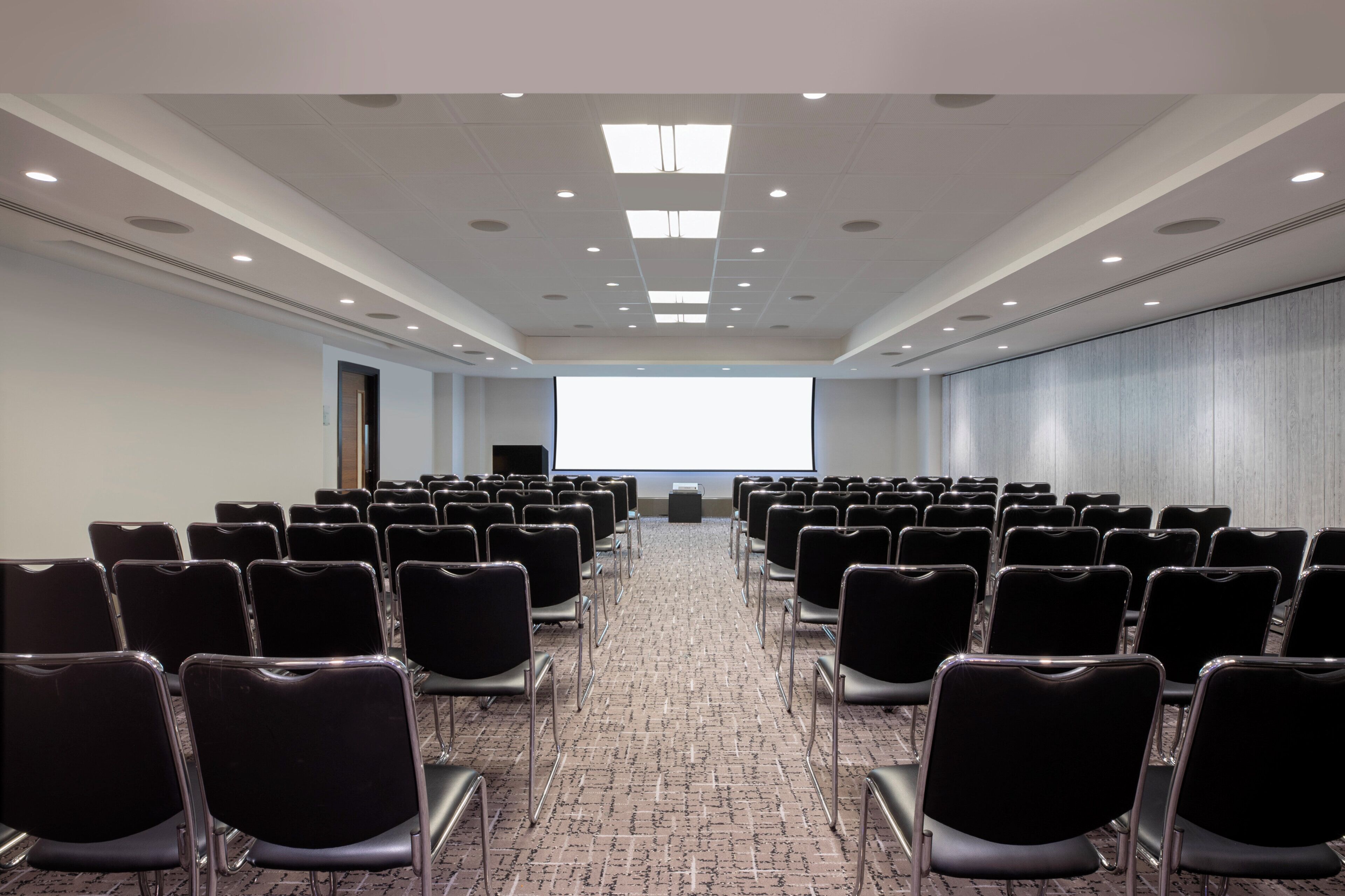 A conference room with rows of chairs, a projector screen, and a carpeted floor.