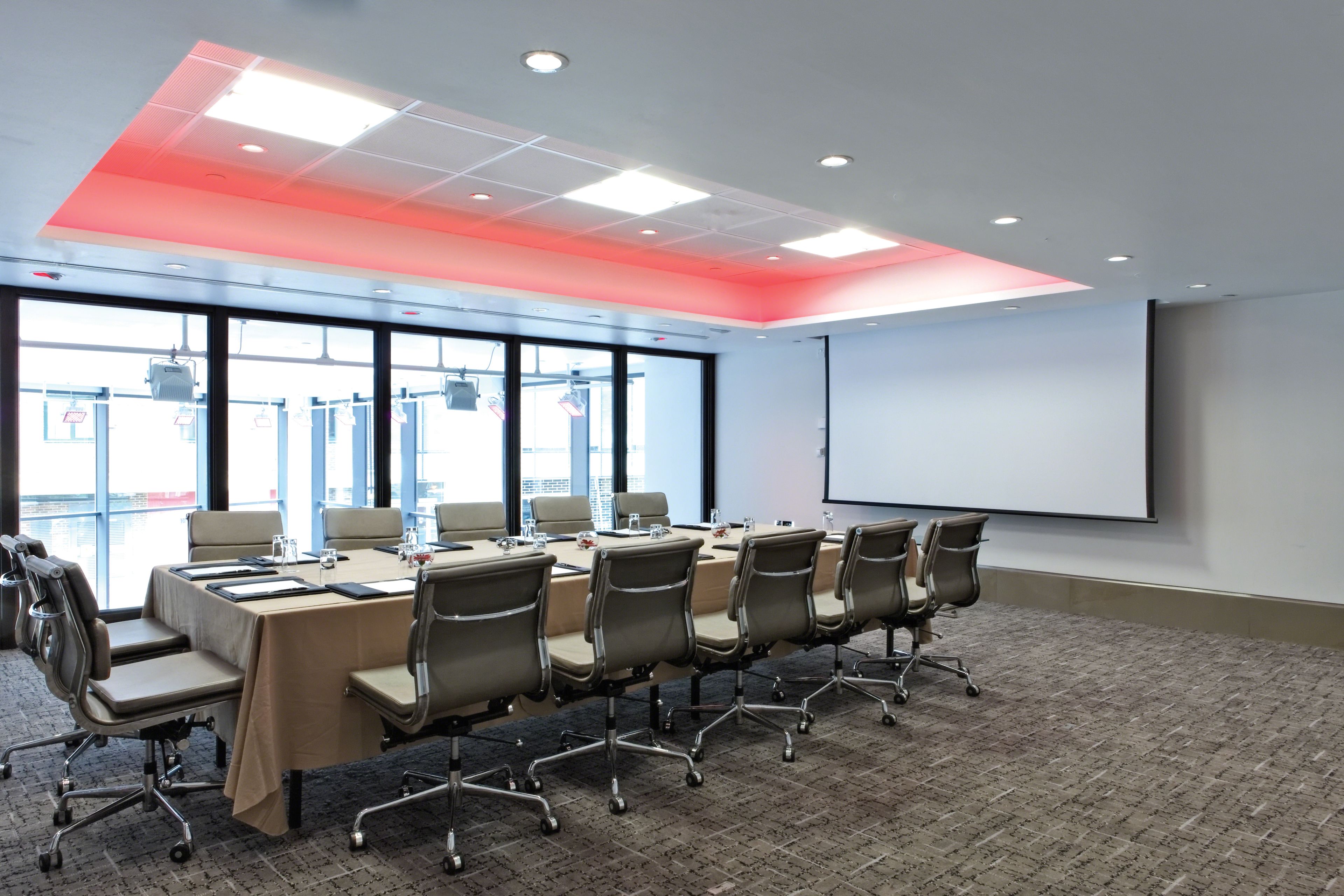A conference room with a long table, chairs, a projector screen, and large windows.