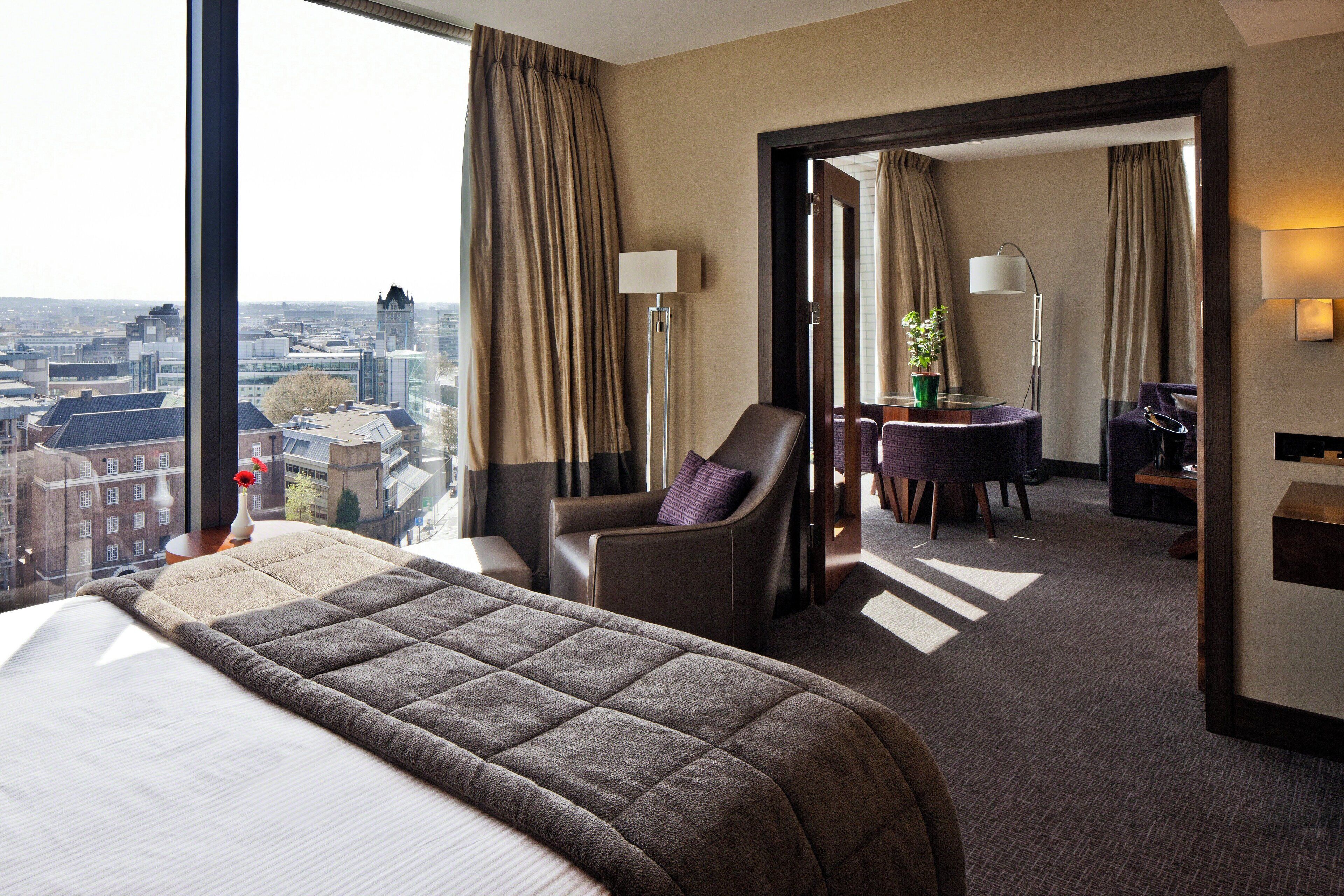 A hotel room with a large bed, a chair, a desk, and a view of the city.