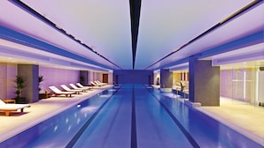 A modern indoor swimming pool with lounge chairs and a glass wall on one side.