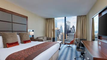 A hotel room with a large bed, a desk, a chair, and a view of the city skyline.