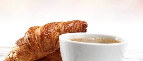 A croissant and a cup of coffee on a white plate with a spoon, set on a wooden table.