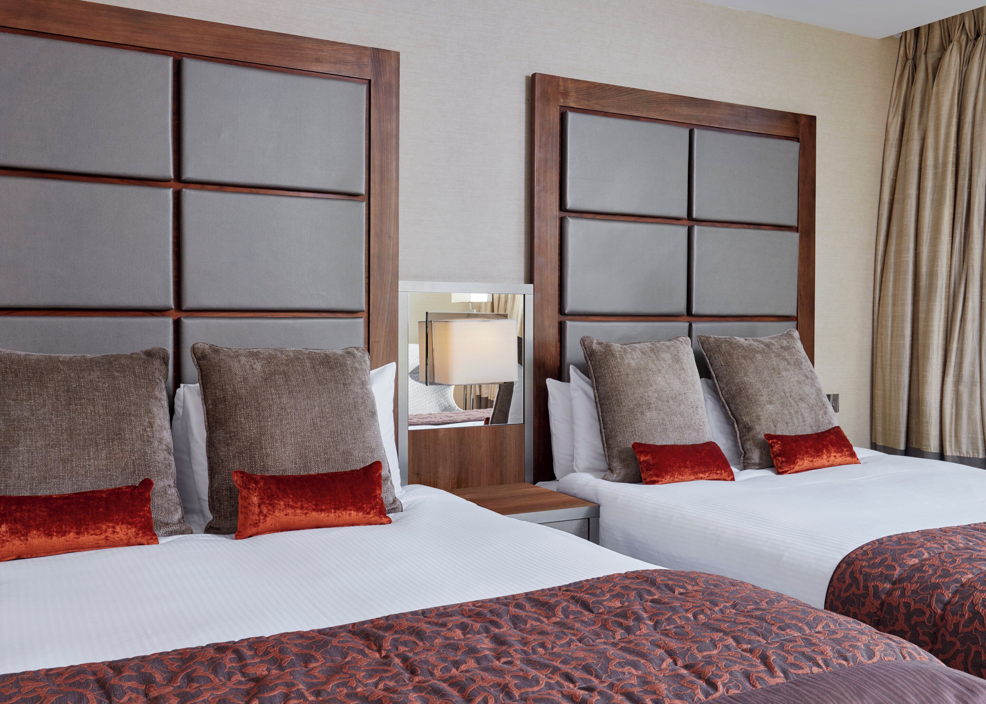 A hotel room with two beds, each with a headboard, white bedding, and multiple pillows.