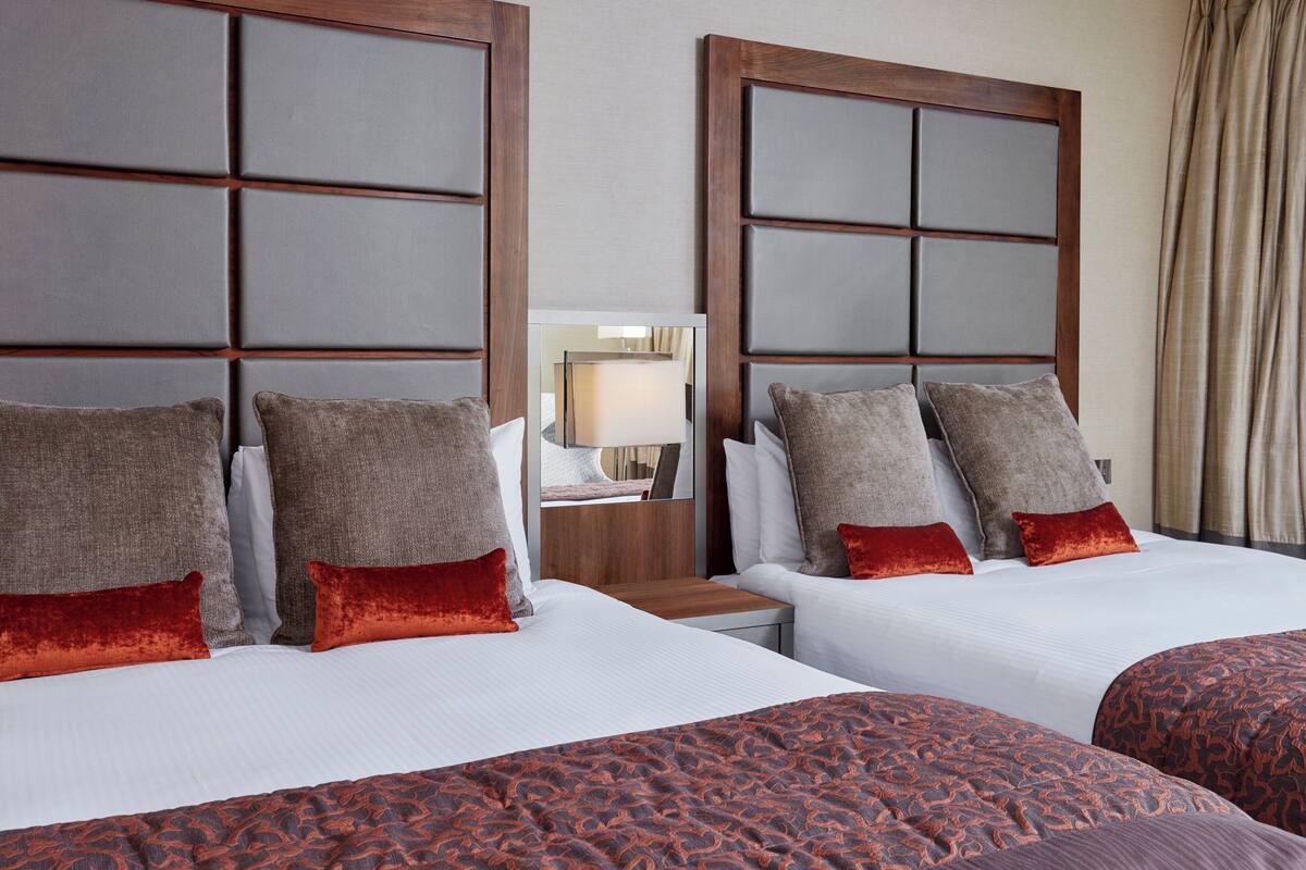 A hotel room with two beds, each with a headboard, white bedding, and multiple pillows.
