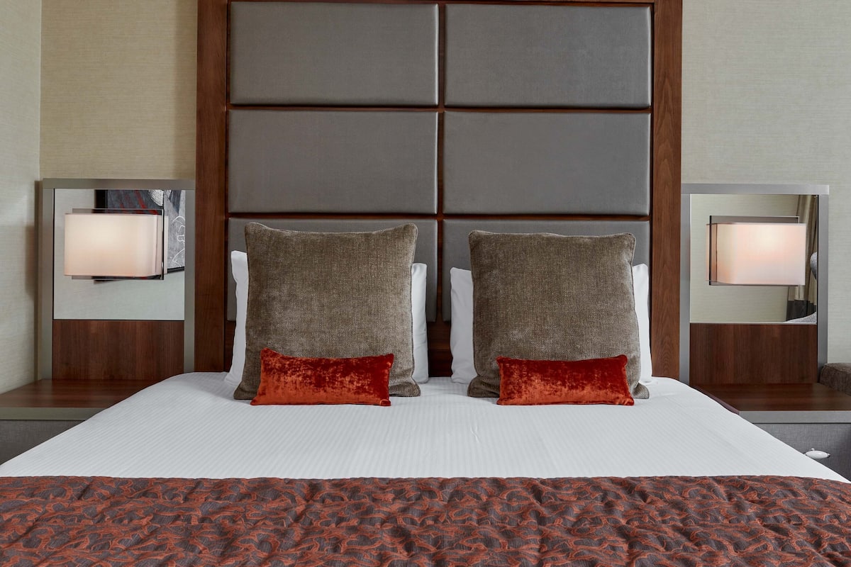 A hotel room with a large bed, two pillows, a patterned blanket, and bedside lamps.