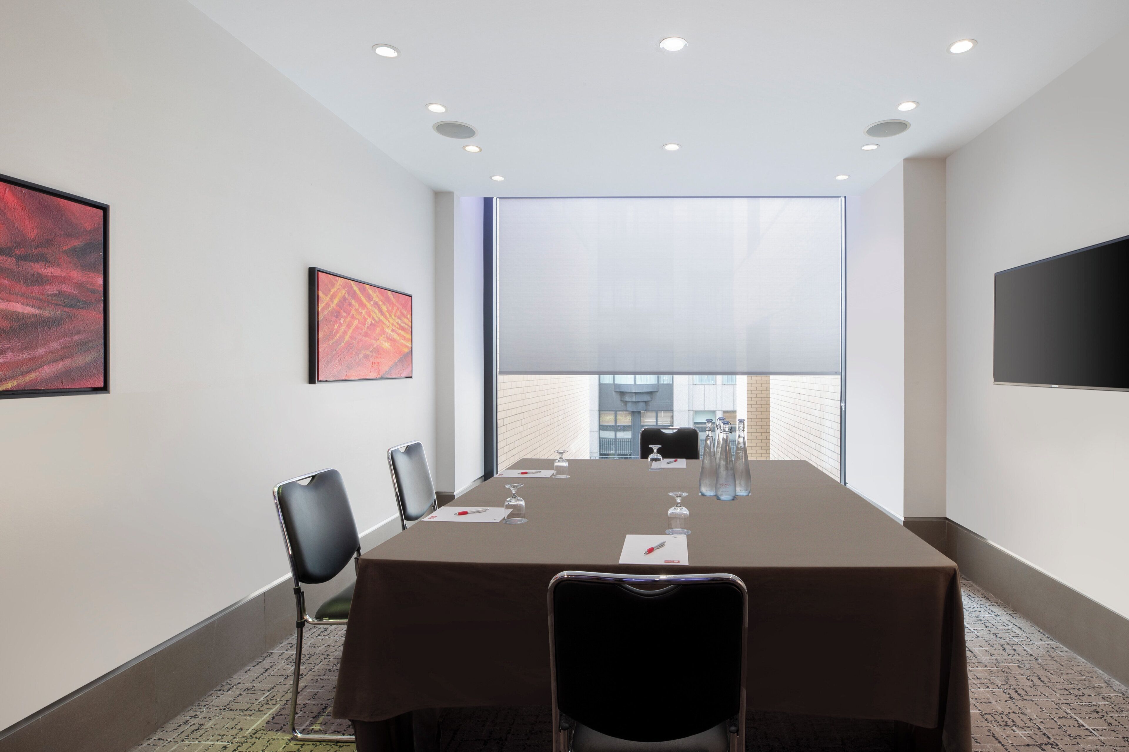 A conference room with a long table, chairs, a projector screen, and artwork on the walls.