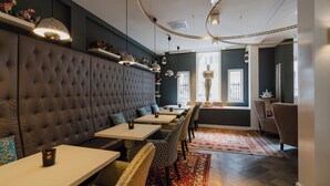 A restaurant with a tufted headboard seating area, white tables, patterned chairs, and a red patterned rug. - Hotel JL No76 (Amsterdam)