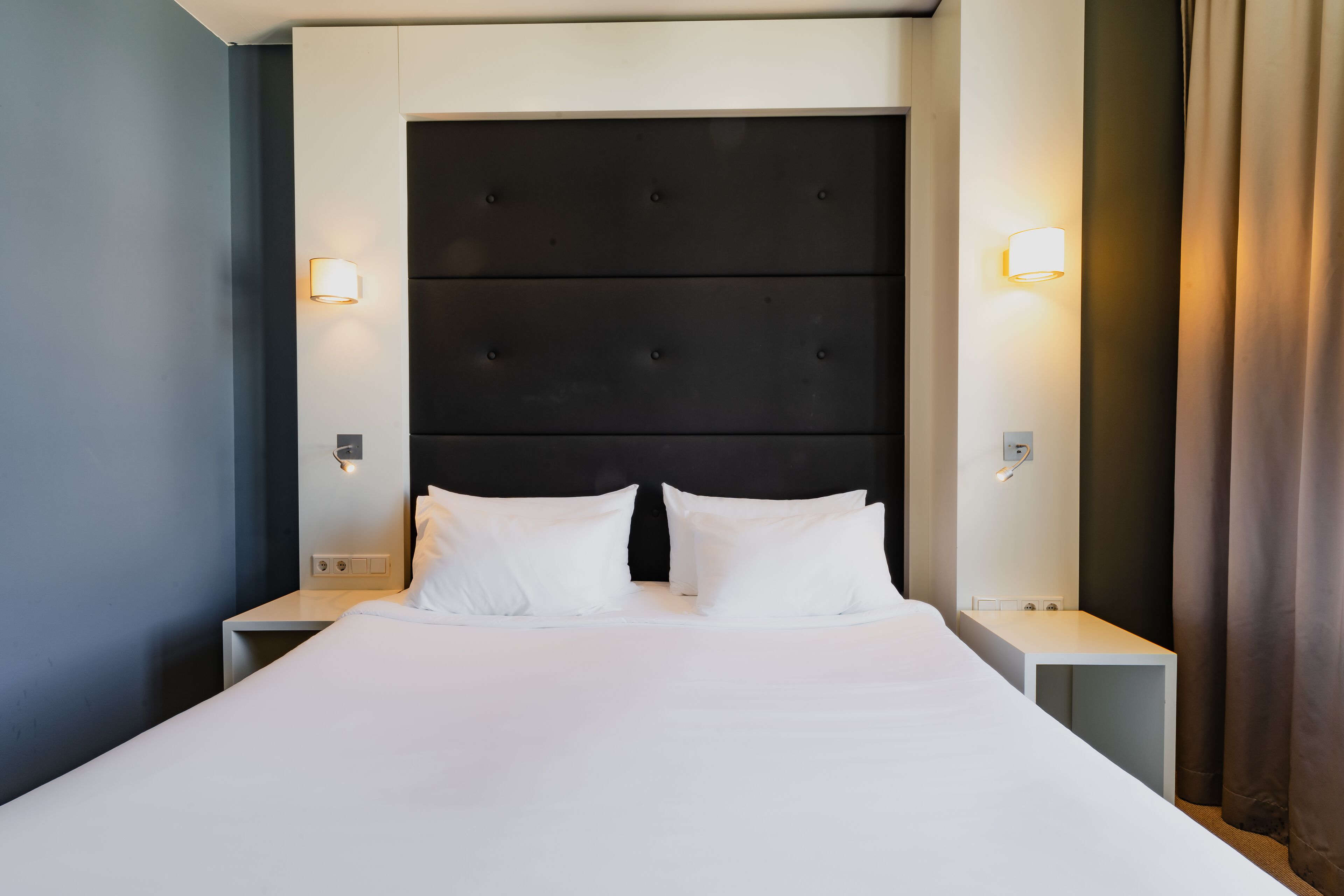 A hotel room with a large bed, two bedside tables, and a dark headboard.