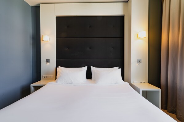 A hotel room with a large bed, two bedside tables, and a dark headboard.