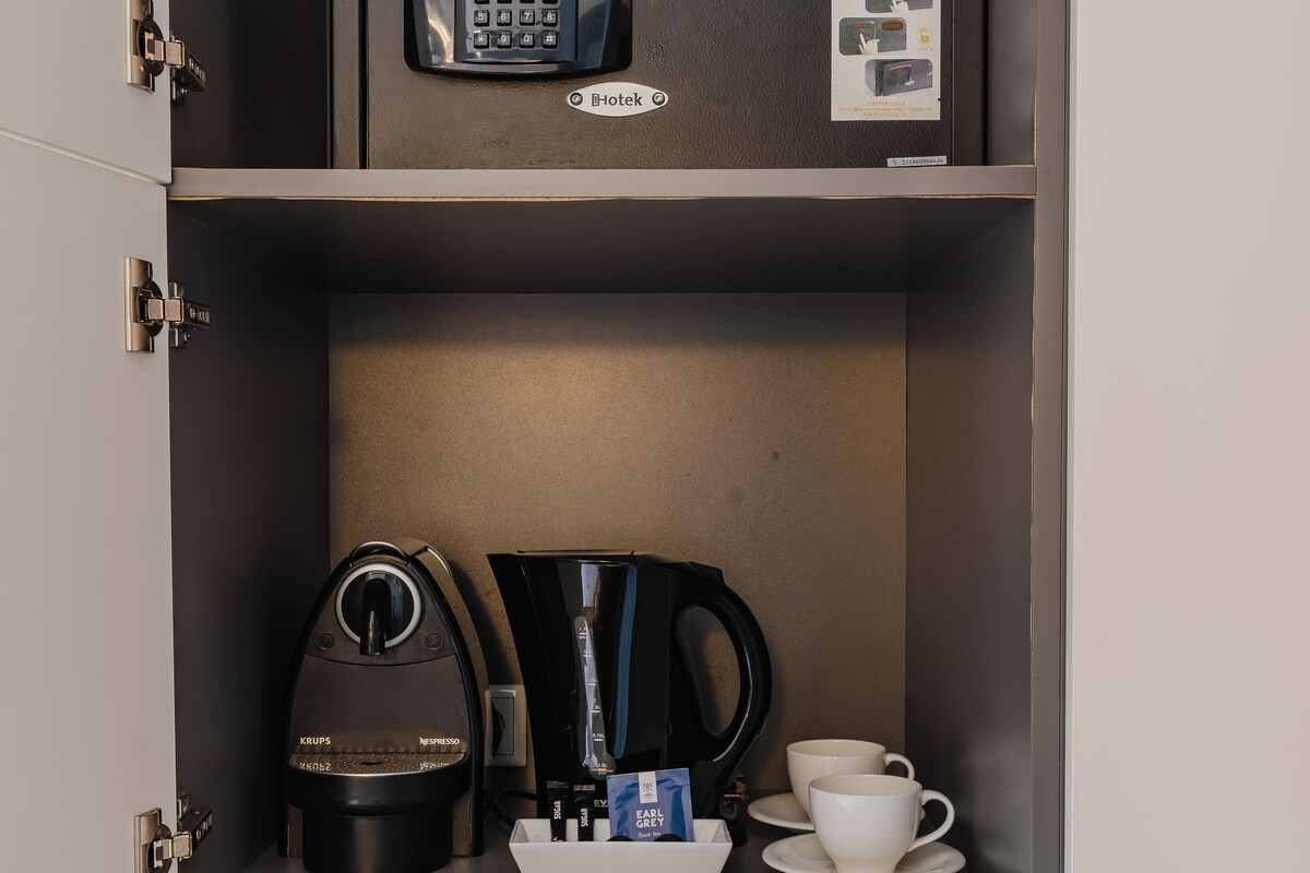 Un minibar con una cafetera, una taza y una caja fuerte pequeña.