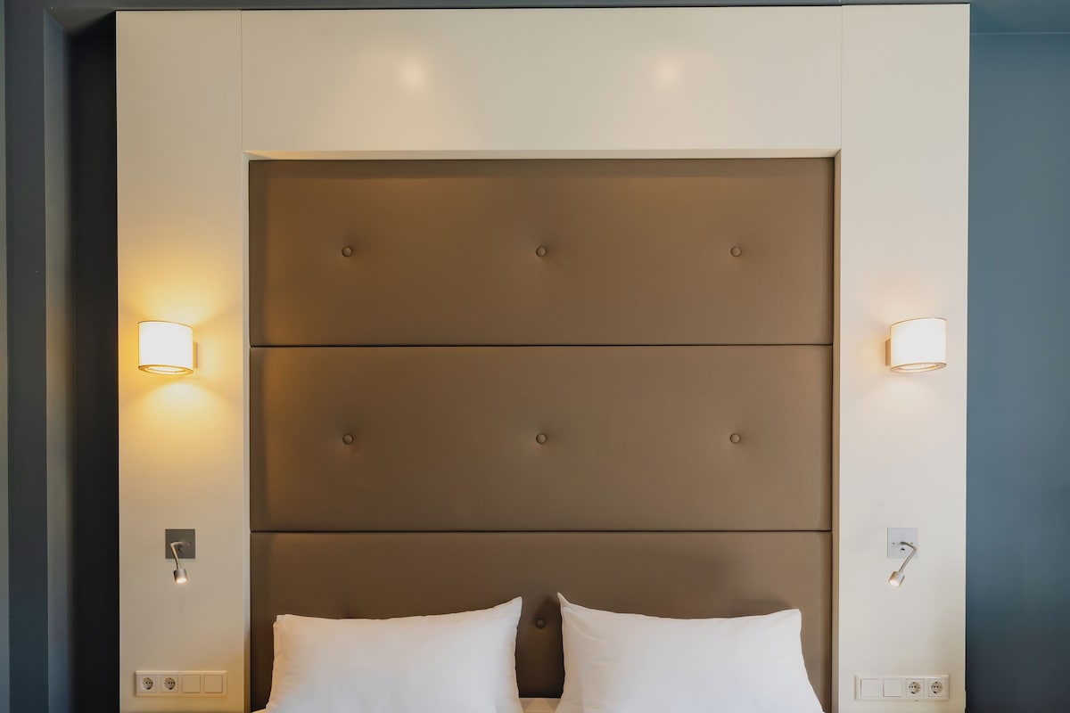 A hotel room with a large bed, two bedside tables, and wall-mounted light fixtures.