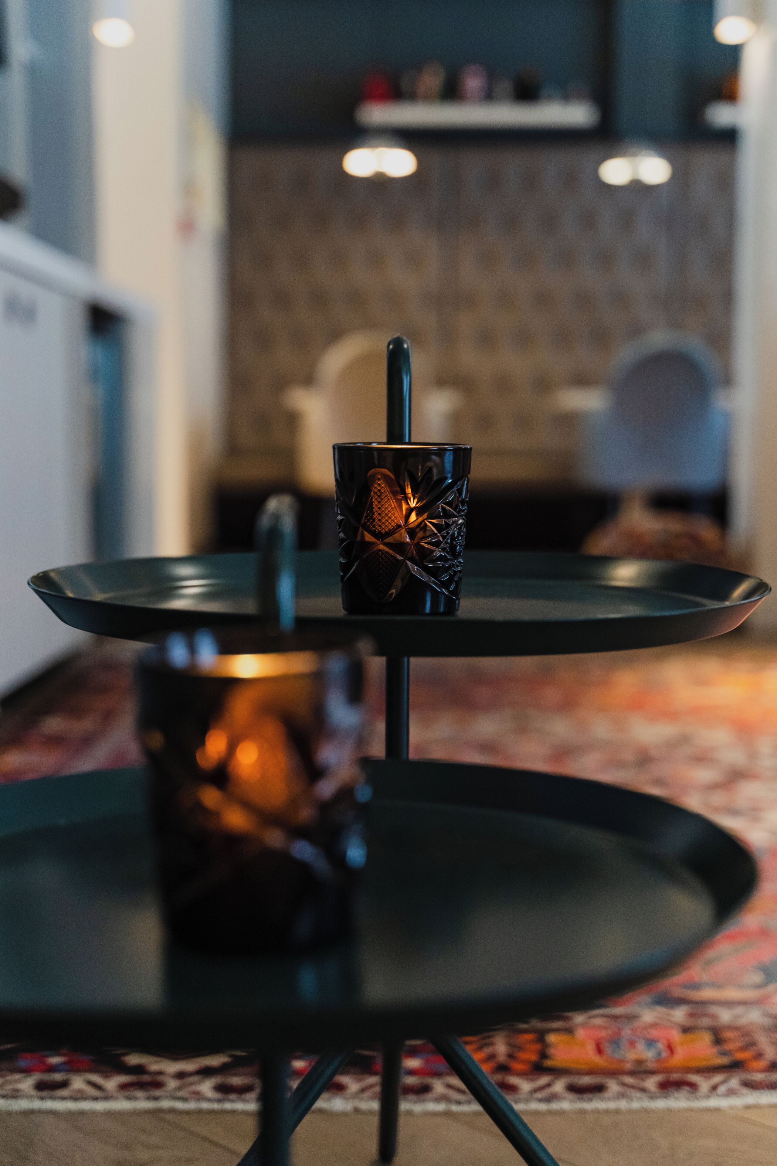 A two-tiered black table with a glass on the top tier and a candle on the bottom tier.