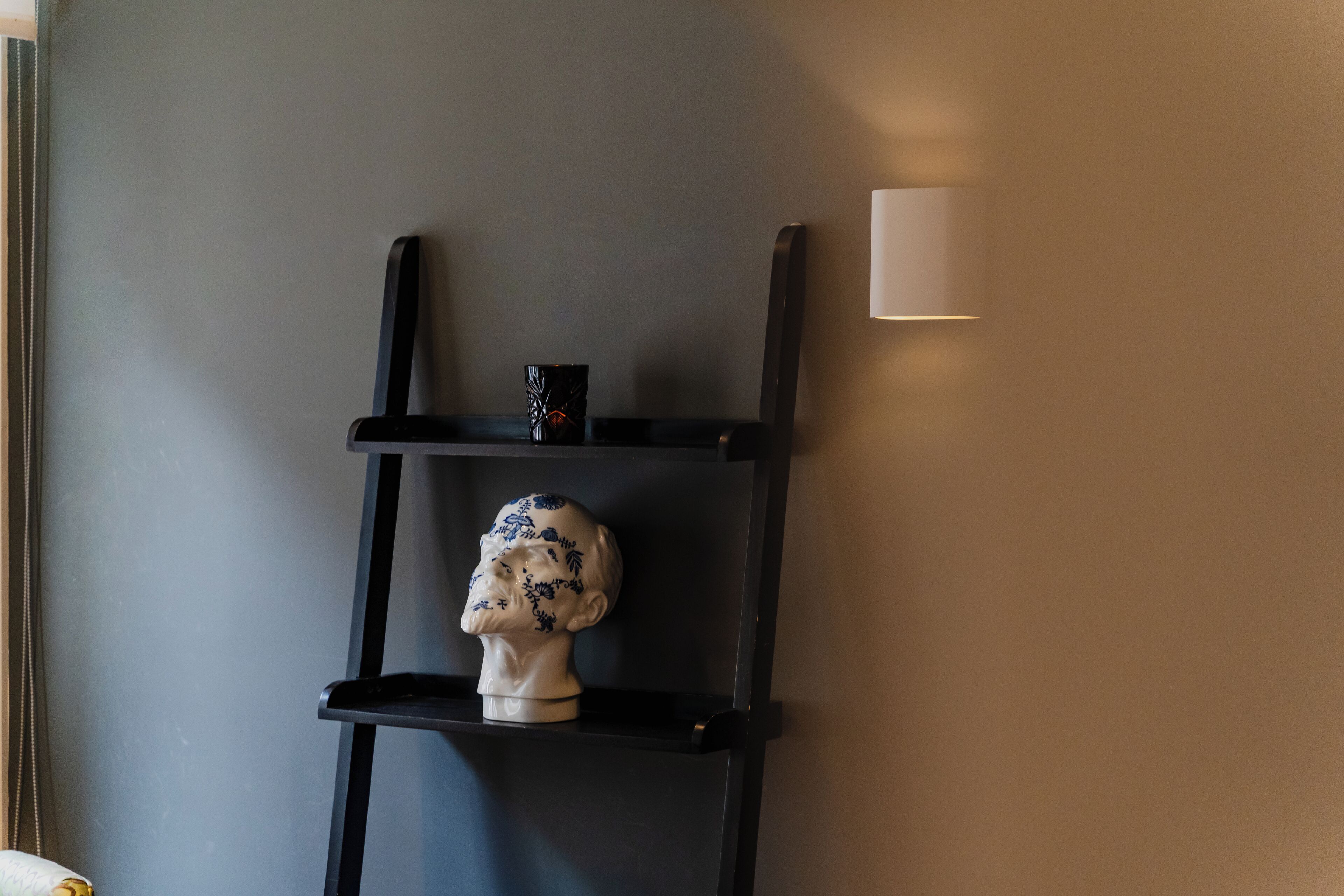 Una estantería negra con un busto y una taza, sobre un pared gris.