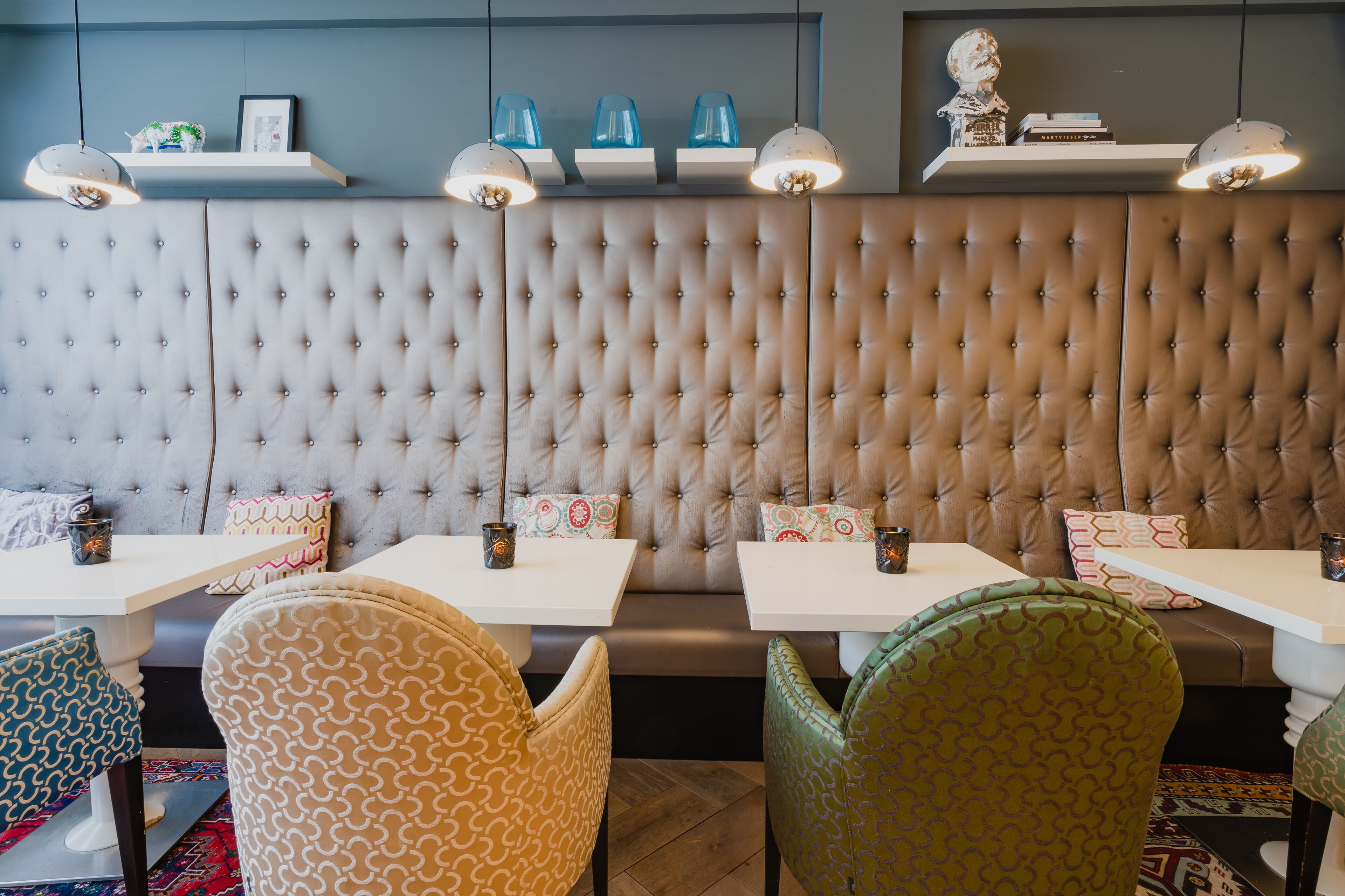 Een restaurant met een ribbelwand, witte tafels, gestreepte stoelen en hanglampen.