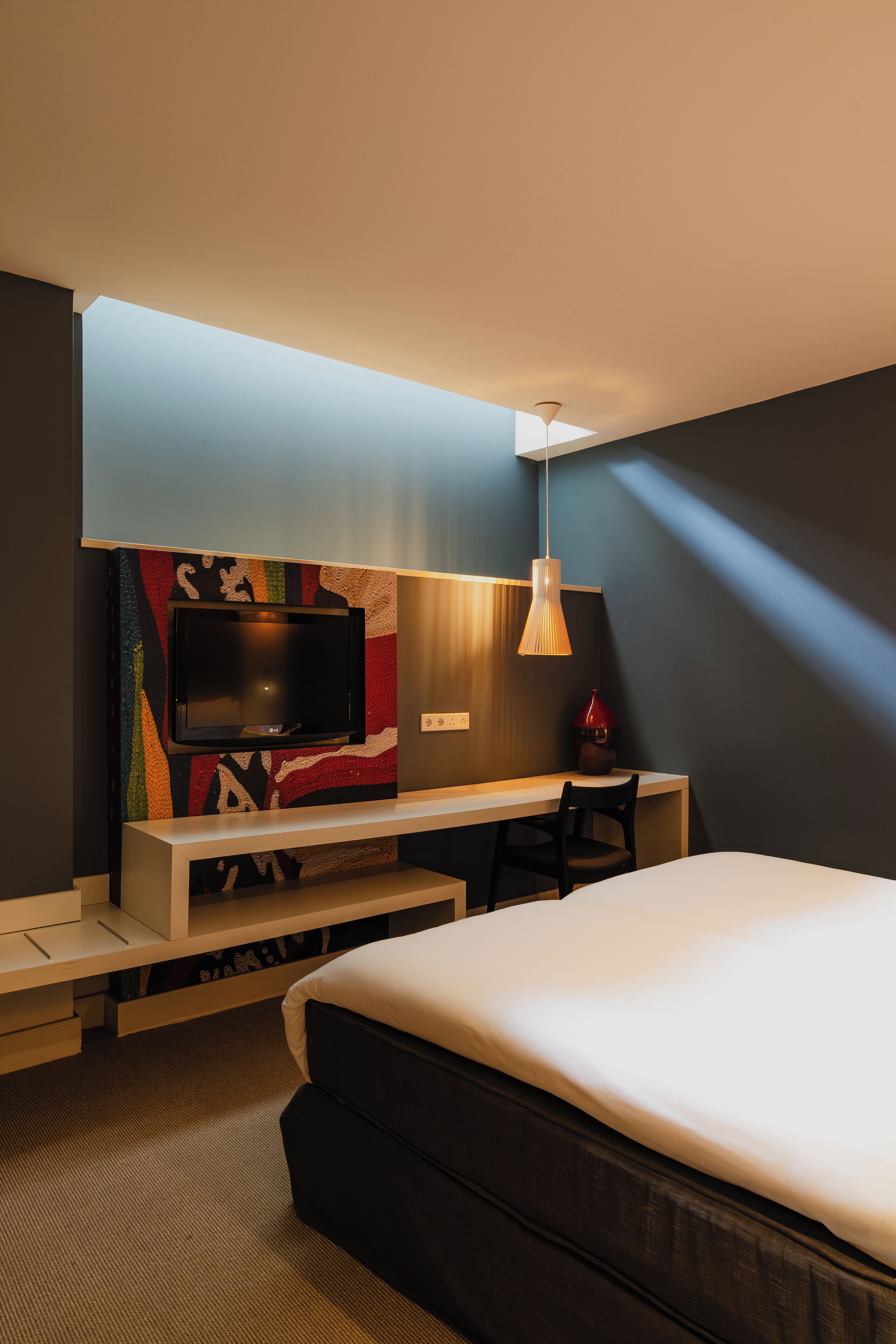 A modern hotel room with a bed, a desk, a television, and a lamp.