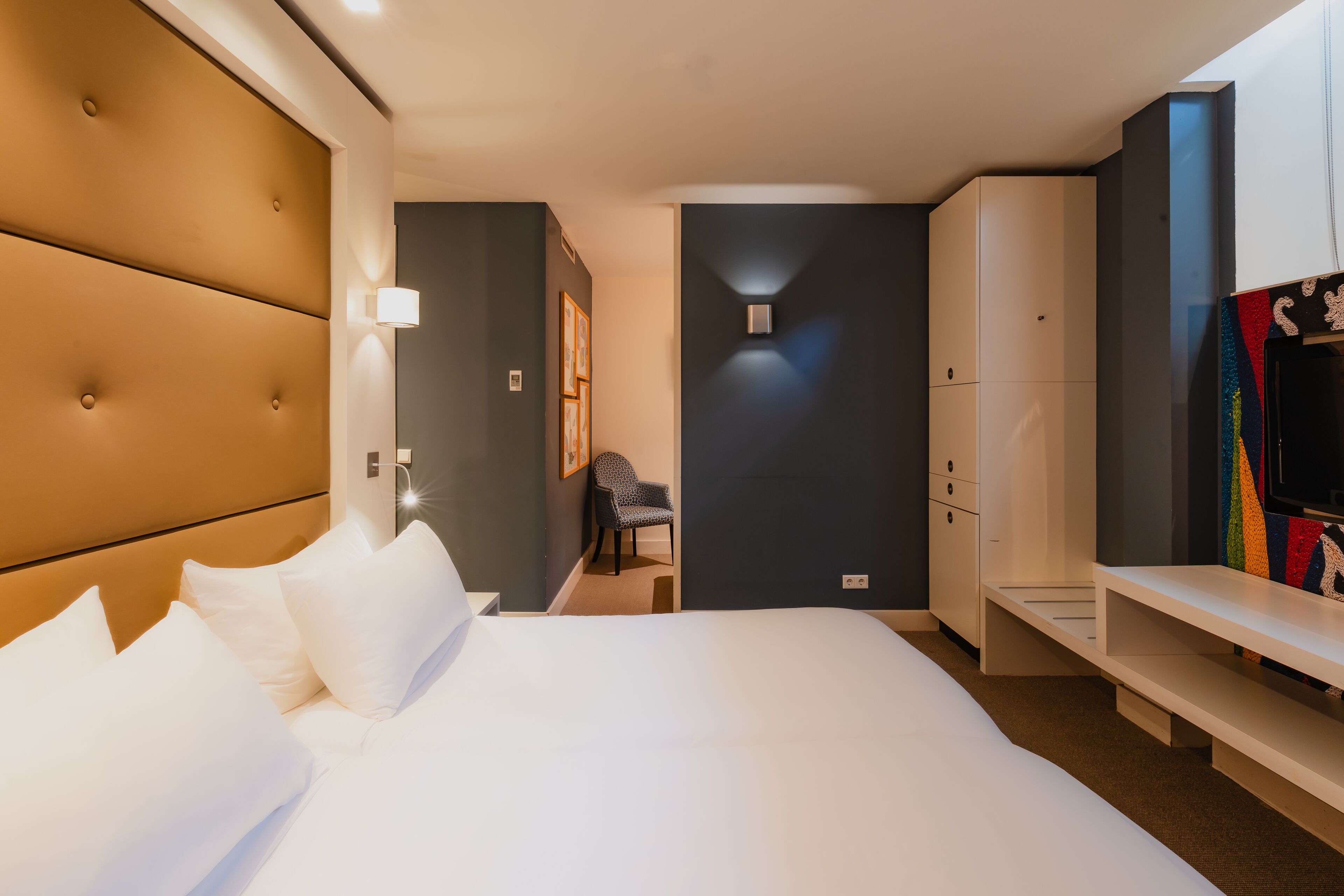 A hotel room with a large bed, a seating area, a wardrobe, and a television.