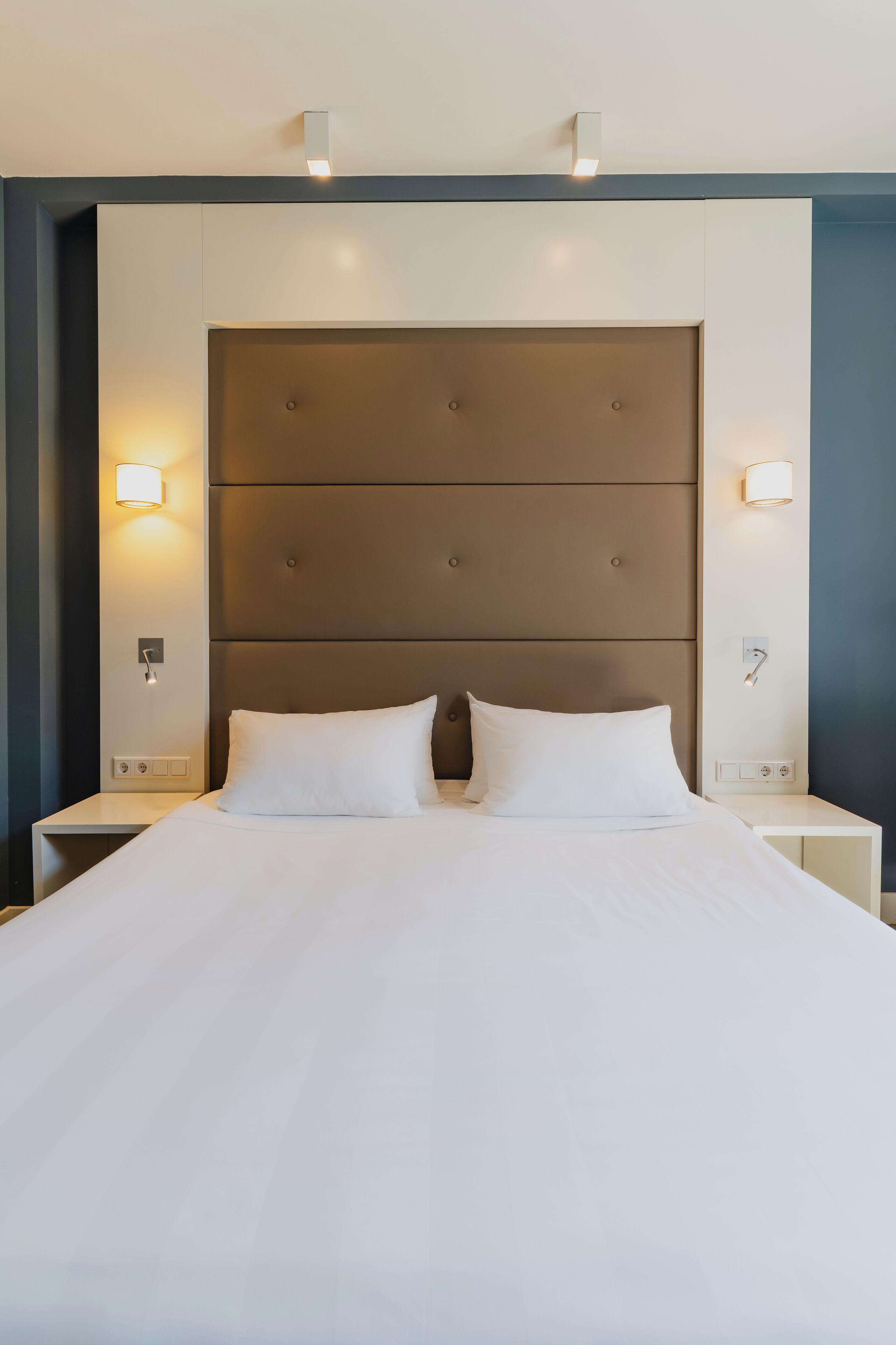 Una habitación de hotel con una cama grande, dos mesitas de noche e iluminación de pared.