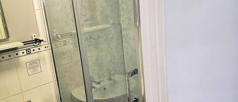 A bathroom with a glass shower enclosure, a sink, and a mirror.