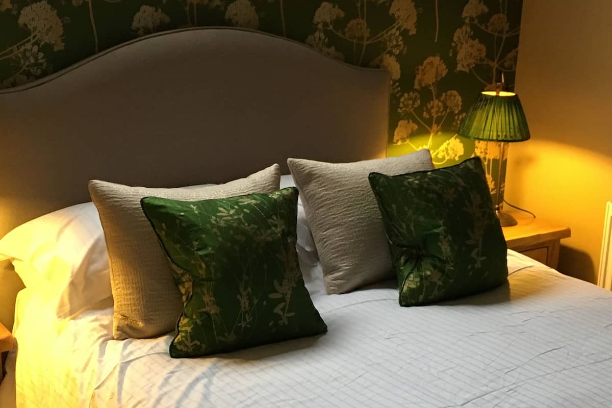 A neatly made bed with white bedding and two green patterned pillows.