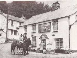 A building with a white facade, multiple windows, and a chimney. There is a horse and rider in front of the building. - The Who'd Have Thought It Inn (Yelverton)